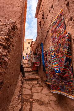 Hanging carpets in a narrow alley in Ait Ben Haddou under soft light and cloudy skies