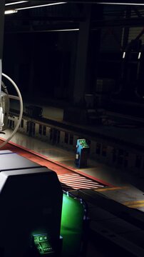 A train station platform is shown at night. The area is mostly empty with a single ticket machine visible. Lights from nearby sources illuminate the space.