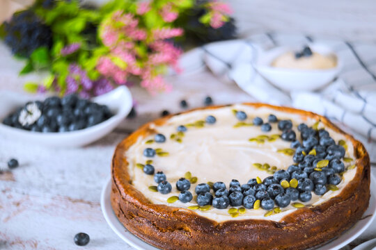 Delicious cheesecake with blueberries on white table with flowers in background