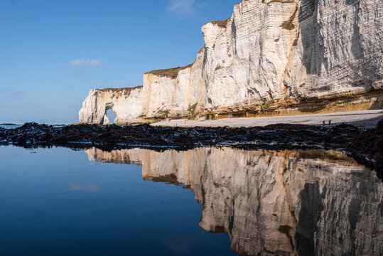 Reflections of white chalk cliffs and natural arches in tidal pools at Etretat coast in Normandy France