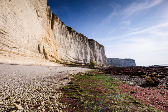 Manneporte cliff stands tall over pebble beach in Etretat, Normandy, France under a blue sky with light clouds