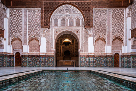 Reflecting pool surrounded by arches and carvings in the courtyard of Ben Youssef Madrasa in Marrakesh, Morocco