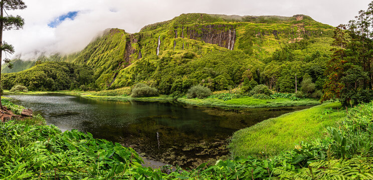 Panoramic view of a volcanic lake surrounded by forest and waterfalls in Flores Island, western Azores, Portugal
