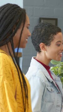 Vertical video: Entering frame, woman in yellow knit and friend in denim walking, pointing at plant