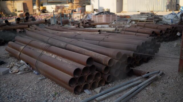 Corroded steel pipes bundled together and lying on a gravel surface at a disorganized construction yard, showcasing weathered industrial materials ready for installation or recycling