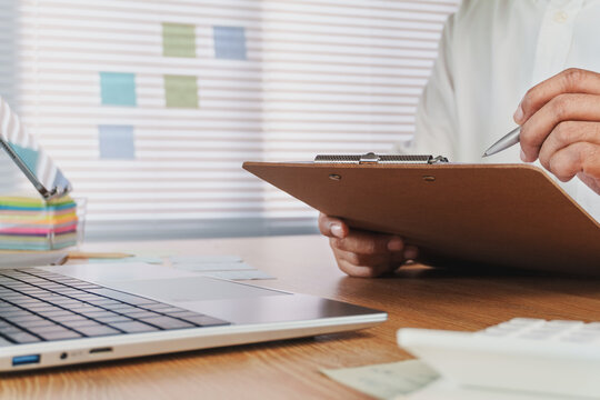 Business Professional Reviewing Documents on Clipboard at Modern Office Desk with Laptop, Sticky Notes and Calculator, Administrative Planning, Financial Audit, Office Workflow and Productivity