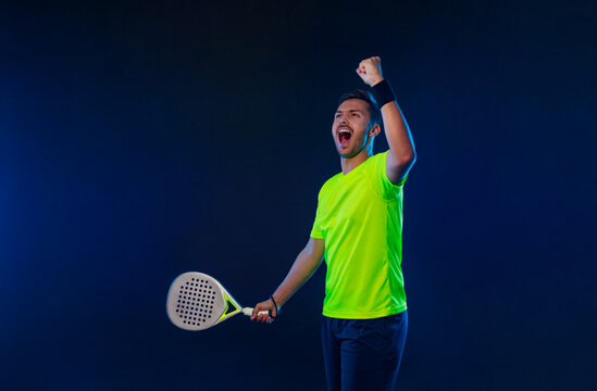 Padel tennis player with racket. Man athlete with paddle racket on court with neon colors. Sport concept. Download a high quality photo for the design of a sports app or betting site.