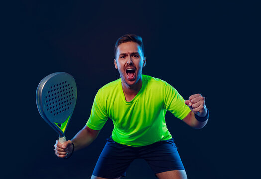 Padel tennis player with racket. Man athlete with paddle racket on court with neon colors. Sport concept. Download a high quality photo for the design of a sports app or betting site.
