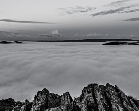 View from Gummers How shows cloud inversion above Lake Windermere in the United Kingdom with rocky foreground and grey skies