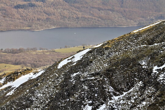 Hiker moves along the ridge to the summit in winter with Coniston Water in the distance in Lake District