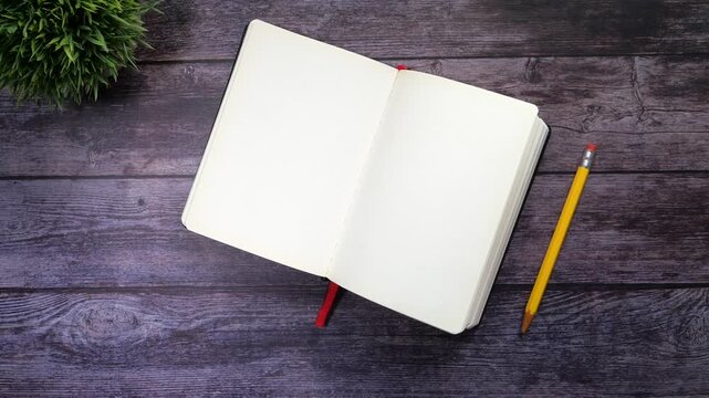Top view of open blank notebook with pencil and plant on dark wooden table