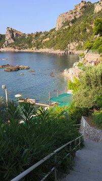 Aerial-like view of La Perla beach in Nerano, Amalfi Coast. Stunning descent down the stairs towards the crystal clear turquoise sea and pebbled shore on a sunny summer day