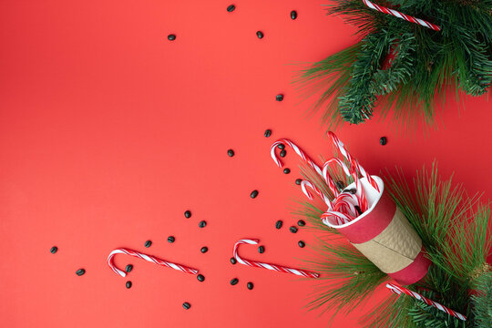 Cheerful, holiday flat lay with paper coffee takeout cup containing coffee beans and candy canes for a peppermint mocha on a bright red background.