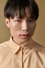 A young Asian man stands confidently, wearing a stylish yellow shirt that highlights his charm. © LIGHTFIELD STUDIOS