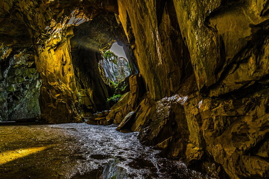 Sunlight beams into an empty chamber of Cathedral Cavern in Little Langdale, revealing its high ceilings and rocky textures in the Lake District