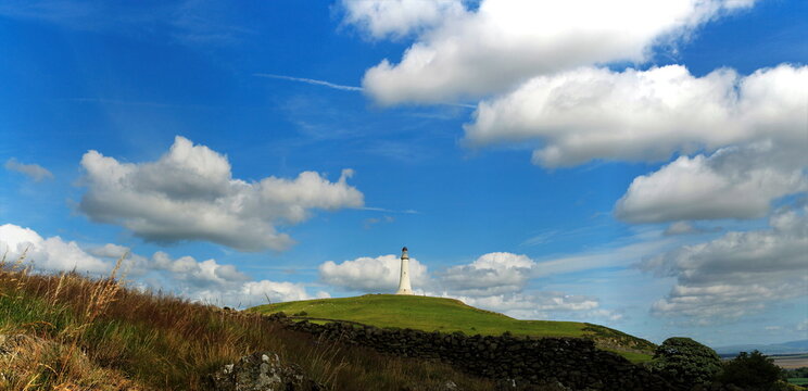 Distant view of Sir John Barrow Monument on Hoad Hill with blue sky and clouds in Ulverston, Cumbria, United Kingdom