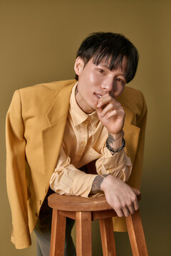 Young man with a trendy outfit playfully leans on a stool, showcasing his fashionable style.