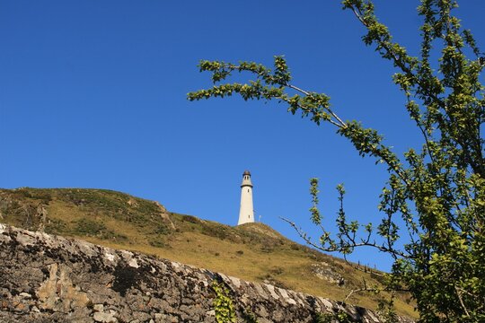 View of the John Barrow Monument from Birkrigg with clear skies and green foliage in the foreground