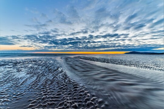 Dramatic sunset view from Walney Island towards distant hills and cloud patterns against the ocean water