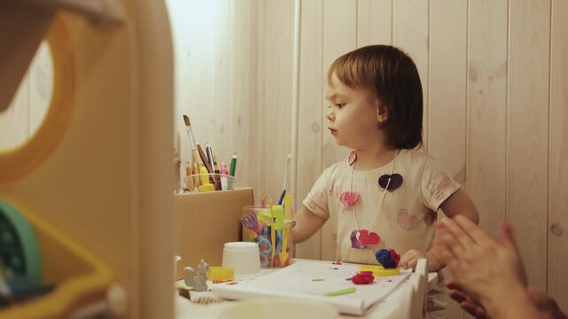 Little girl enjoying creative play at a small desk in her bedroom with toys and warm light.