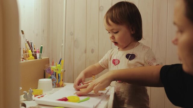 Little girl exploring colorful toys at a play table while spending creative time with her mother.