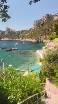 Aerial-like view of La Perla beach in Nerano, Amalfi Coast. Stunning descent down the stairs towards the crystal clear turquoise sea and pebbled shore on a sunny summer day