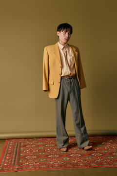 A young man in a unique yellow blazer stands on a colorful rug.