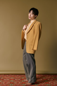 A handsome young Asian man poses confidently in a stylish outfit, exuding charm and elegance.