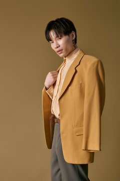 A young Asian man strikes a confident pose in a striking yellow blazer, showcasing modern fashion.