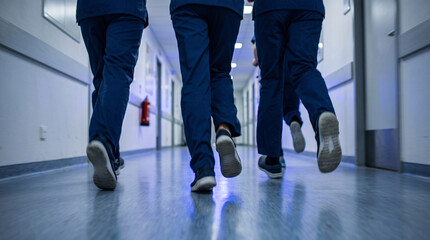 Fototapeta premium Back view of a medical team running down a hospital corridor in motion blur, emergency crisis and blue alert code concept, focus on doctors' legs and scrubs in a minimalist clinic interior