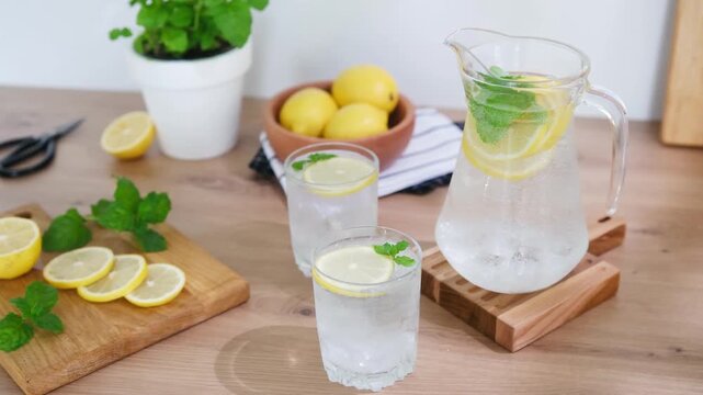 Refreshing lemonade pitcher and glasses with mint and lemon slices on a wooden surface