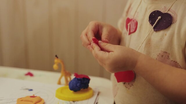 Close-up of toddler hands molding colorful clay figures on a small desk during indoor play.