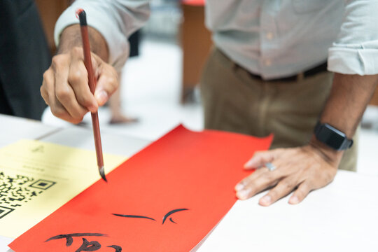 Focused student in blazer writing traditional Chinese calligraphy characters with ink brush on vibrant red paper, demonstrating authentic cultural heritage and tactile craftsmanship