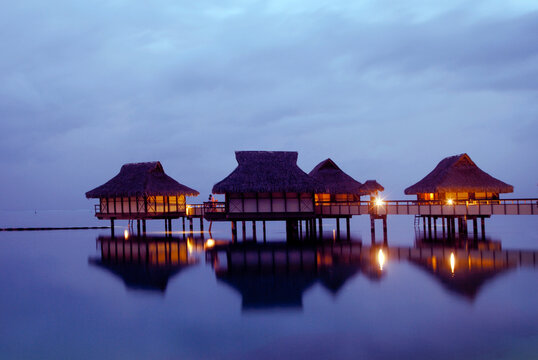Bungalows on stilts at dusk with lights glowing over water in South Pacific