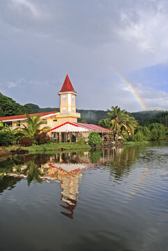 Rainbow arches over church in Uturoa with reflection in water on Raiatea island in French Polynesia