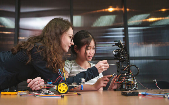 Teacher mentors a student assembling a robotics project in a STEM classroom, encouraging engineering skills, coding, teamwork, and hands-on innovation.