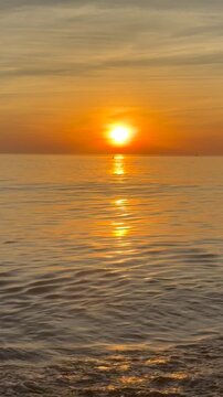 Golden sunrise over calm sea with distant boat silhouette crossing horizon. Warm sunlight reflects on gentle waves, creating scenic, cinematic seascape with peaceful morning atmosphere and coastal bea