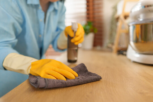 Woman wipes a wooden kitchen countertop with disinfectant spray and a microfiber cloth, promoting hygiene, sanitation, and efficient household cleaning in a modern home.