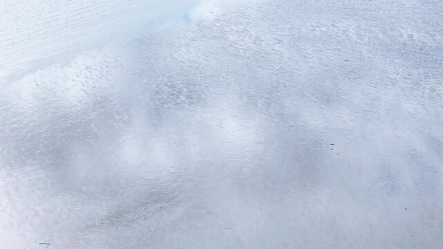 Abstract aerial view of wet sand ripples and shallow tidal water in Normandy, France. Minimal coastal texture with soft reflections and natural low tide pattern