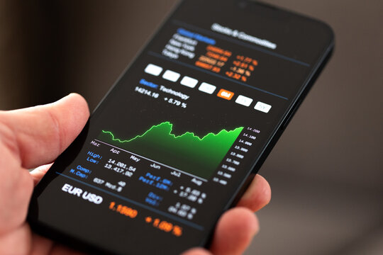 Hand holds a smart phone, stock markt information, rising technology chart and data on the display. Financial markets themes, graph moving up, growth, business, investment idea, market data.