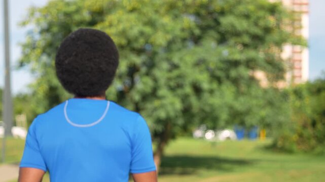 Latin American athlete with afro hair looking back with pride while walking in urban park with building background daytime
