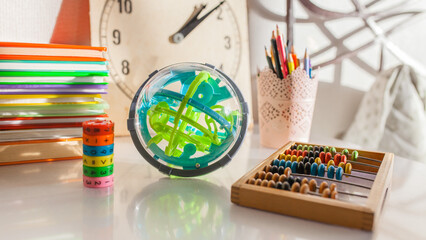 Various educational toys and learning supplies on table: spherical puzzle, wooden abacus, stack of books, math learning cube. Childhood education, development, cognitive learning, school preparation. © Natallia