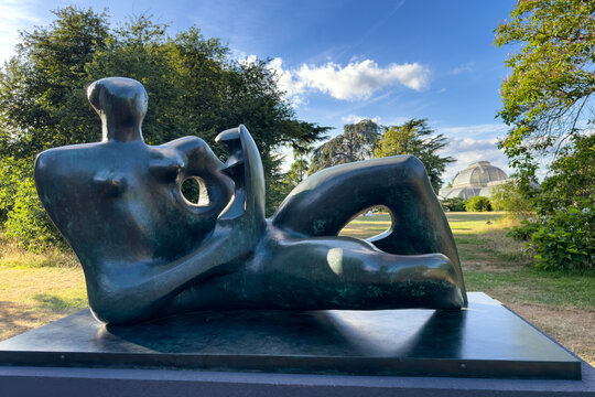 London, UK - 4 July 2026: Reclining Mother and Child, , Henry Moore giant bronze sculpture from 1975 - 1976, in the grounds of Kew Gardens, south London, with the glass Palm House behind.