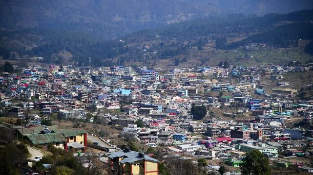 A wide scenic establishing shot of a densely populated hilly town Champawat, Uttarakhand with colorful houses built on slopes.
