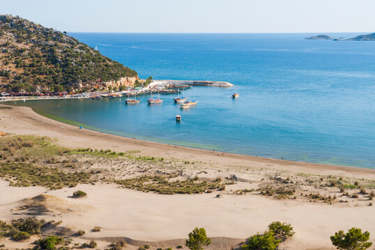 Waves gently lap on sandy shore as boats rest in creek near beach in Turkey overlooking blue sea and hills