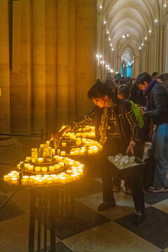 Woman lights a candle in Notre Dame Cathedral in Paris as part of her prayer and reflection during a busy time in the historic location