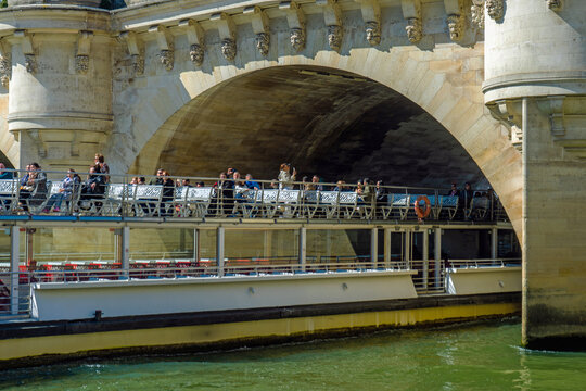 Tourist boat sails under Pont Neuf in Paris during a bright winter day with people enjoying the view