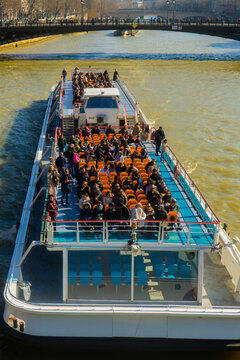 Tourist boat travels on river Seine on sunny winter day in Paris, France enjoying the city views and warm sunlight