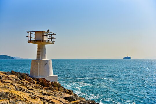 Lighthouse stands by the sea near Mount Johnston with a ship passing in the distance on a clear day in Hong Kong