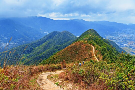 Hikers walk on the Tai To Yan Ridge Trail in Hong Kong, China with mountain views and cloudy sky